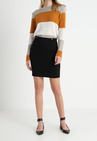 Strickpullover mit orange, grau und cremefarbenen Streifen, kombiniert mit einem schwarzen, taillierten Rock. Schwarze Absätze vervollständigen das Outfit. Strukturierter Stoff durchgehend.