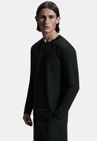 Must have a black long-sleeve shirt with a round neckline, made of smooth fabric. Şirtin ön kısmında ince bir logo var ve dar kesim kolları var.