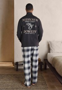 Czarny długi rękaw z białym napisem i grafiką z tyłu. Szare i białe spodnie piżamowe w kratę. Gładki materiał, swobodny krój.