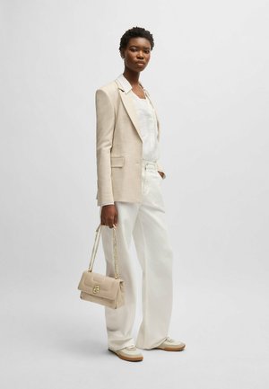 Beige linen blazer over a white top, paired with white wide-leg trousers and beige sneakers. Holding a small beige bag with a gold chain strap.