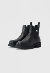 Bottines Chelsea en cuir noir avec une large semelle en caoutchouc, des panneaux élastiques sur les côtés et une languette à l'arrière. Comprend une étiquette avec logo.