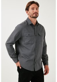 Grijs langemouwen shirt met knoopsluiting aan de voorkant, twee borstzakken en een gladde, zachte textuur. Het shirt heeft een klassieke kraag en een rechte zoom.
