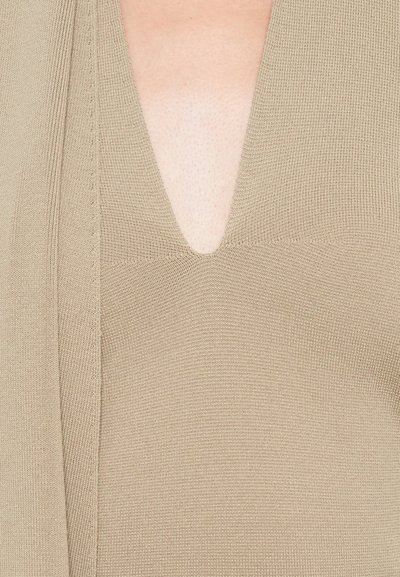 Beige knitted V-neck sweater showing upper chest and detailed stitching along the neckline and shoulder.
