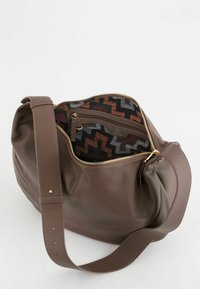 Bolso de cuero marrón con acabado texturizado, cuenta con una cremallera dorada y un forro de tela estampada en tonos tierra. Incluye una correa ancha ajustable.