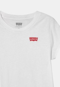 Camiseta de algodón blanca con escote redondo, mangas cortas y un logo rojo de Levi's en el lado izquierdo del pecho, con una textura suave y agradable al tacto.