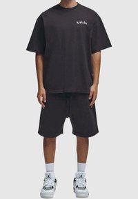 T-shirt noir à manches courtes avec un col rond et un texte imprimé en blanc, accompagné d'un short noir assorti et de chaussures de sport blanches.