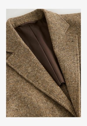 Bruine tweed blazer met een gestructureerde weving, notch-lapels en een bruine binnvoering. Geen zichtbare knopen; op maat gemaakte ontwerpdetails zijn aanwezig.