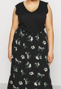 Top senza maniche nero con scollo a V abbinato a una lunga gonna nera caratterizzata da un motivo floreale verde e rosa. Gonna con vita elastica.