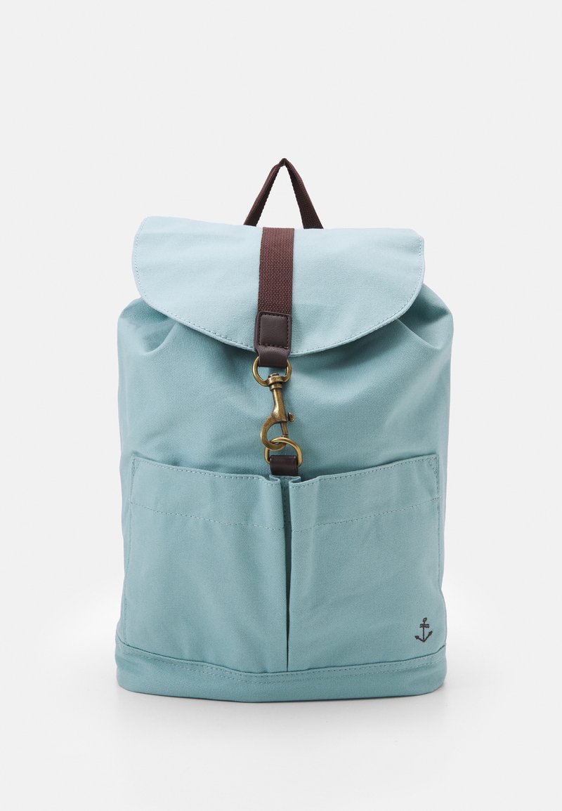 Helleblaue Stoff-Rucksack mit braunem Riemen, Messingverschluss, zwei Vordertaschen und kleinem Ankerlogo in der unteren rechten Ecke.