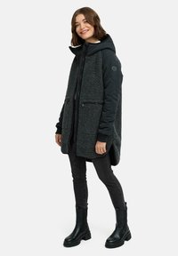 Svart och grå fleecefodrad jacka med huva, blixtlåsfickor, texturerad kropp, släta ärmar, kombinerad med mörka jeans och svarta stövlar.