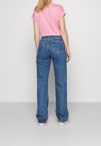Camiseta rosa de mangas enrolladas combinada con unos vaqueros de pierna recta azules que cuentan con dos bolsillos traseros y una textura de denim desgastado. Zapatillas blancas.