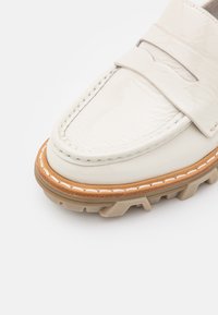 Mocassins en cuir verni blanc avec une tige texturée, des détails en couture et une semelle contrastante brun clair avec des motifs de traction.