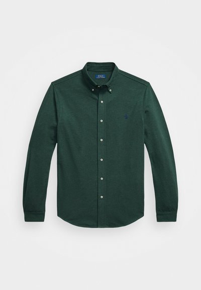 Camisa de botones de manga larga en verde oscuro con cuello abotonado y pequeño logo bordado en el lado izquierdo del pecho, sobre un fondo blanco.