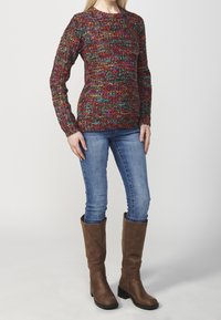 Multikleurige gebreide trui met een textuurpatroon, lange mouwen en een ronde halslijn, gecombineerd met blauwe jeans en bruine kniehoge laarzen.