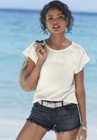Top testurizzato color beige chiaro con maniche corte, abbinato a pantaloni shorts in denim scuro. Una borsa intrecciata e una cintura blu chiaro completano il look.