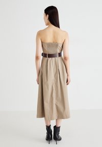 Beige bezramienkov dress s naťahovacím zadným dielom, stiahnuté tmavo hnedým opaskom, siahajúce po polovicu tela. Kombinované s čiernymi členkovými topánkami.