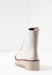 Valkoinen nahkainen nilkkasaapas, jossa on teksturoitu viimeistely, hopeanvärinen metallinen vetoketju ja paksu sahalaitainen pohja.