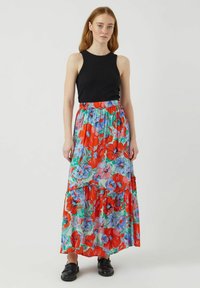 Falda maxi con estampado floral en tonos rojos, azules y verdes, con un diseño en capas y cintura elástica; combinada con una camiseta sin mangas negra.