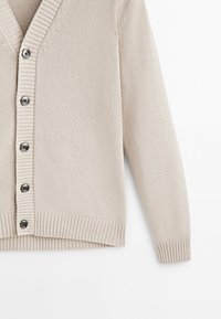 Cardigan beige en maille avec un col en V, un col côtelé et des poignets côtelés, et six boutons foncés sur le devant. Texture douce et coupe décontractée.