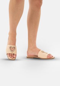 Beige instappers met open teen, voorzien van een hartvormige rhinestoneaccent en een platte zool, ontworpen voor comfort.