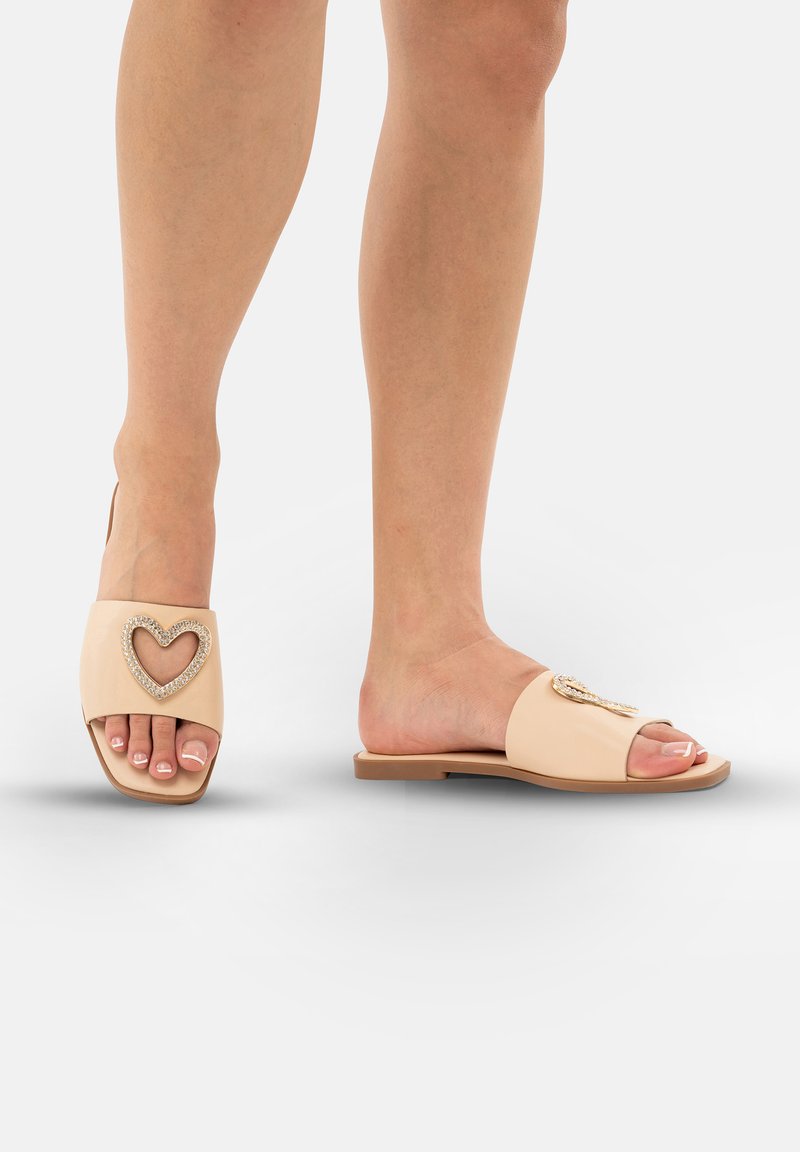 Beige instappers met open teen, voorzien van een hartvormige rhinestoneaccent en een platte zool, ontworpen voor comfort.