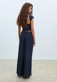 Pantaloni a gamba larga blu navy con vestibilità sartoriale, dotati di tasche posteriori e dettaglio con bottone, abbinati a un top blu fitted.