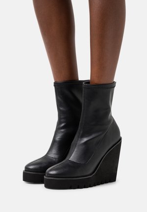 Bottes basses en cuir noir avec une semelle compensée et une finition lisse, dotées d'un bout arrondi et de coutures apparentes.