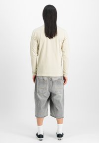 Camisa de manga larga beige claro combinada con pantalones cortos de mezclilla grises. Los pantalones cortos cuentan con dos bolsillos traseros y un ajuste holgado y relajado. Zapatillas negras visibles.