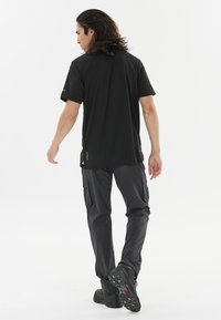 Sort kortærmet t-shirt kombineret med mørke cargo-bukser. Stoffet virker letvægtigt, med en afslappet pasform og diskret detaljer på siderne.
