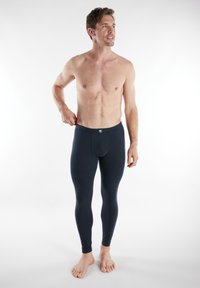 Leggings neri realizzati in un materiale elastico, con un design aderente e una cintura elasticizzata. La modella è in piedi a piedi nudi.