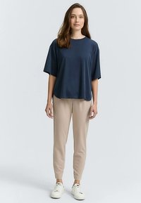 Haut bleu marine à manches courtes en tissu doux, associé à un pantalon beige fuselé. Le mannequin porte des baskets blanches ; design minimaliste sans motifs.