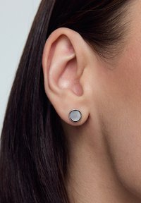 Srebrna kolczyk w kształcie okręgu z błyszcząca, gładką powierzchnią i czarną metalową obręczą, umieszczony w małżowinie usznej.