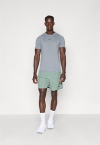 Camiseta deportiva gris de manga corta con logo negro, combinada con pantalones cortos verde claro con un logo de swoosh negro, completada con zapatillas blancas.