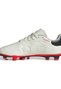 Zapato de fútbol blanco con superficie texturizada, acentos rojos, talón negro y cordones grises, diseñado para un rendimiento óptimo en campos de hierba.