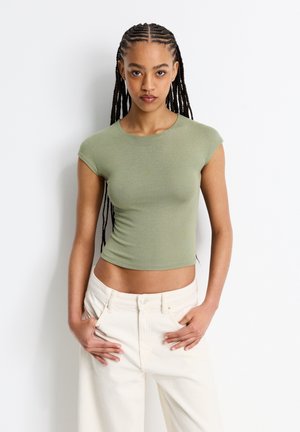 Kortærmet, tætsiddende grøn top lavet af let jersey-stof. Har en rund halsudskæring og et cropped design. Bæres sammen med højtaljede hvide jeans.