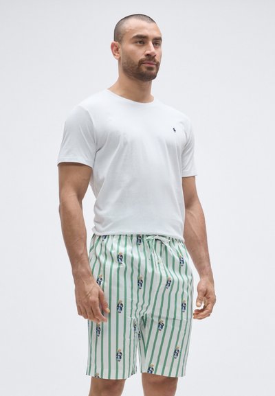 Λευκό βαμβακερό t-shirt σε συνδυασμό με πράσινα και λευκά ριγωτά μαγιό με μικρές εικονογραφημένε�ς φιγούρες. Ελαστική μέση με κορδόνι.