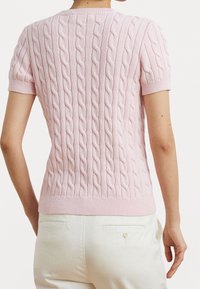 Růžový pletený svetr s krátkými rukávy, s copánkovým vzorem a žebrovaným lemem. Záda mají hladkou texturu a jemné detaily.