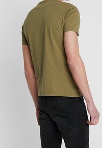 Olijfgroene T-shirt met korte mouwen, gemaakt van zacht katoen, met een ronde halslijn en een relaxte pasvorm, gecombineerd met zwarte taps toelopende broek.