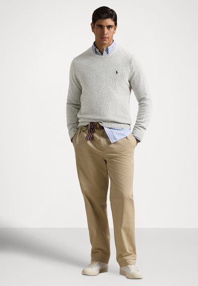 Svetlosivo pleten pulover z rebrastimi manšetami čez svetlomodro srajco s črtami. Obleko dopolnjujejo bež hlače chino in beli supergi. Priložnostna zasnova.