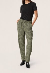 Groene joggerpants met luipaardprint, voorzien van een elastische tailleband en zijzakken, gecombineerd met een zwart T-shirt met korte mouwen en zwarte haklaarzen.