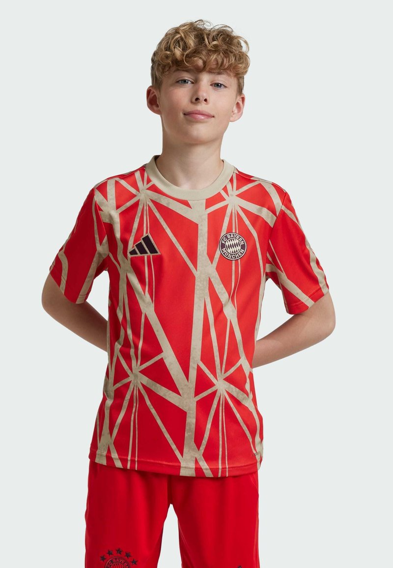 Camiseta de fútbol roja con patrón geométrico crema, cuello redondo, mangas cortas, con un logo bordado en el pecho.