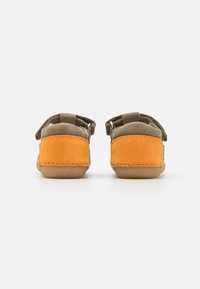 Scarpe per bambini con un design in suede verde e arancione, dalla forma arrotondata, con cinturino a strappo e dettagli cuciti. Suola in morbida gomma.