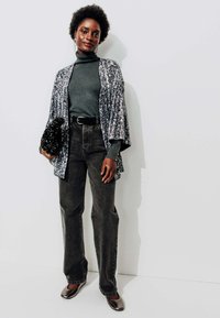 Pull à col roulé gris foncé, cardigan ouvert pailleté, jeans noirs et chaussures métalliques, accompagné d'une pochette en perles noires. Textures lisses.