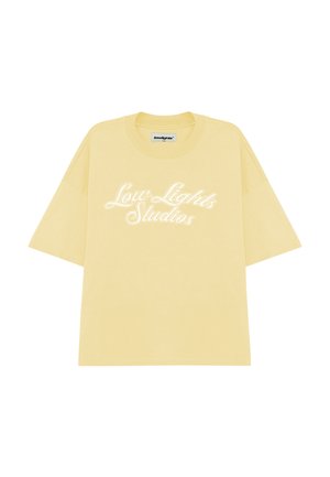 T-shirt en coton jaune à manches courtes, avec le texte "Low Lights Studios" en lettres cursives blanches sur le devant.