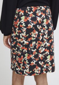 Jupe à motif floral avec des nuances de noir, rouge, vert et crème ; fabriquée en tissu doux ; présente une coupe ajustée et une taille.