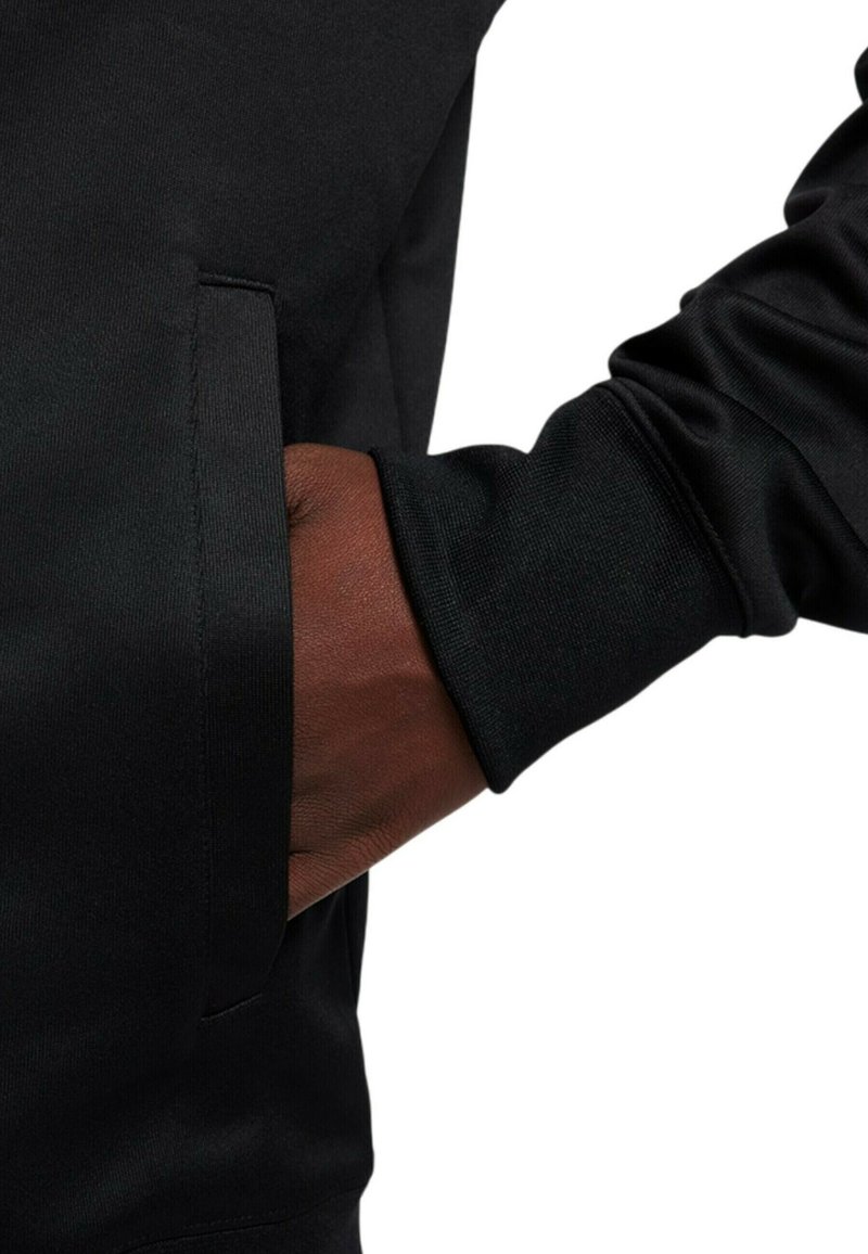 Dunkelhäutige Hand in die Seitentasche eines schwarzen Kleidungsstücks mit langen Ärmeln und geripptem Bündchen gesteckt.