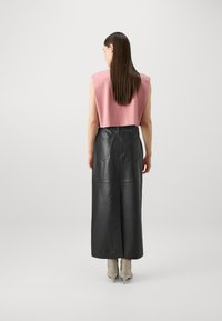 Afskåret lyserød ærmeløs top parret med en lang sort læderskirt med baglommer, glat tekstur og højt livdesign.