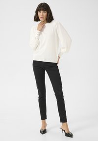 Bílý pletený svetr s nabíranými rukávy a knoflíkovými detaily na manžetách, kombinovaný s dobře padnoucími černými džíny a špičatými černými špičatými mules na podpatku.