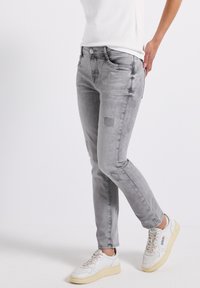 Grijze spijkerbroek met een slim fit, met patchdetails op de knieën, en gestyled met een wit shirt en witte sneakers.