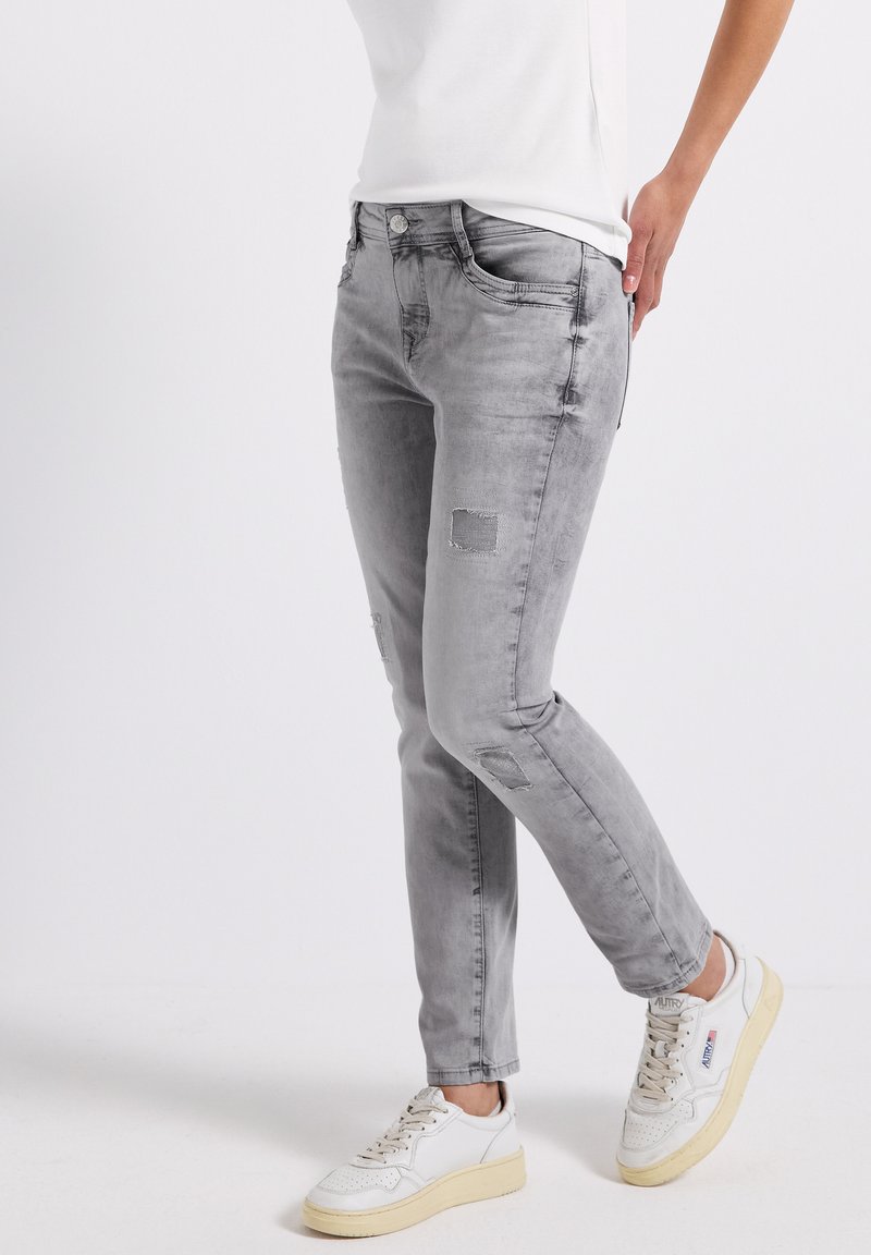Grijze spijkerbroek met een slim fit, met patchdetails op de knieën, en gestyled met een wit shirt en witte sneakers.